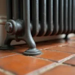 Pied de radiateur fonte avec embouts protecteurs en caoutchouc posé sur carrelage en terre cuite ancien