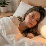 Femme qui se réveille paisiblement grâce à une alarme lumineuse simulant le lever du soleil dans une chambre scandinave