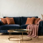 Salon chic avec canapé bleu marine en velours associé à des coussins terracotta et un jeté rose poudré sur tapis en jute naturel